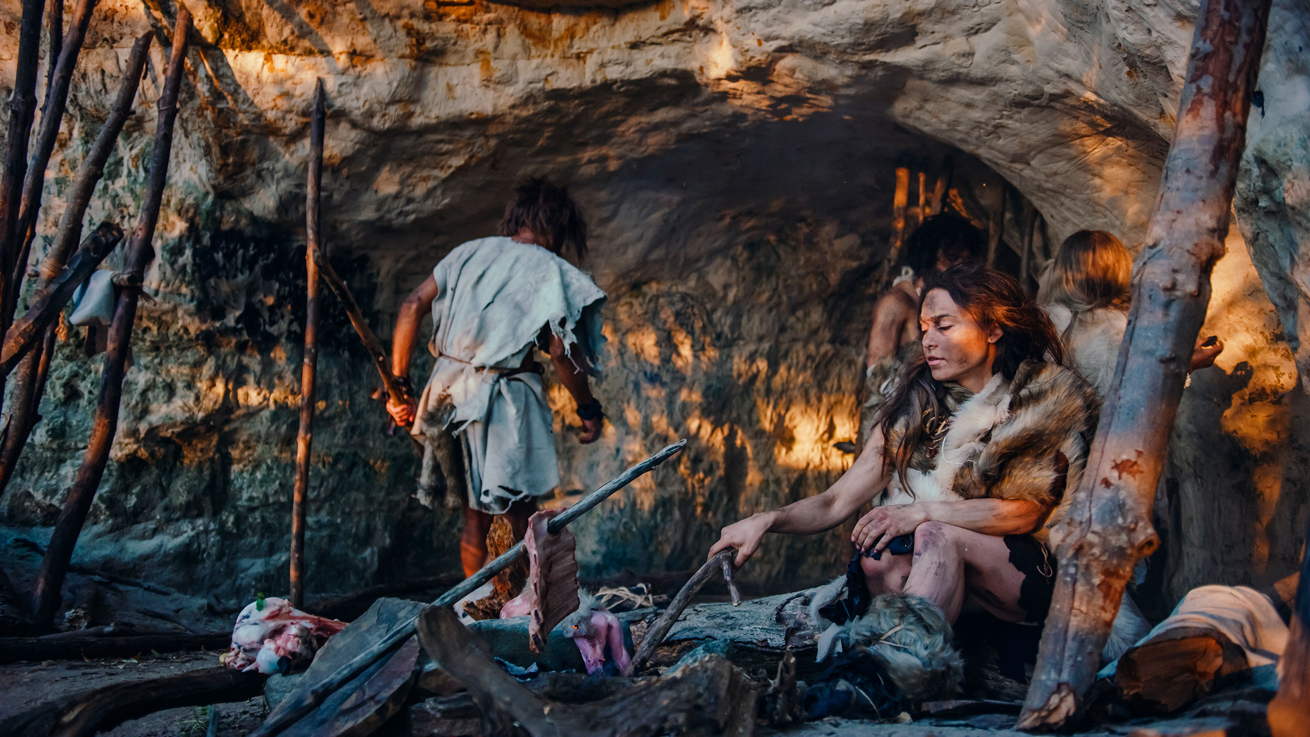 Hombres y mujeres prehistóricos cocinando en una cueva