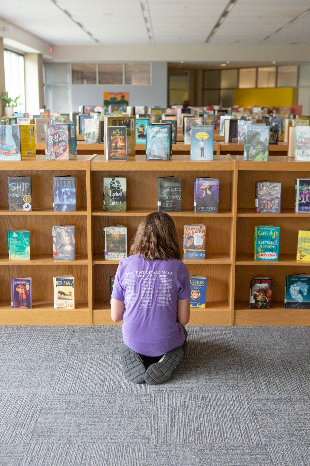 En la imagen puedes ver una niña arrodillada de espaldas, mirando una estantería de libros