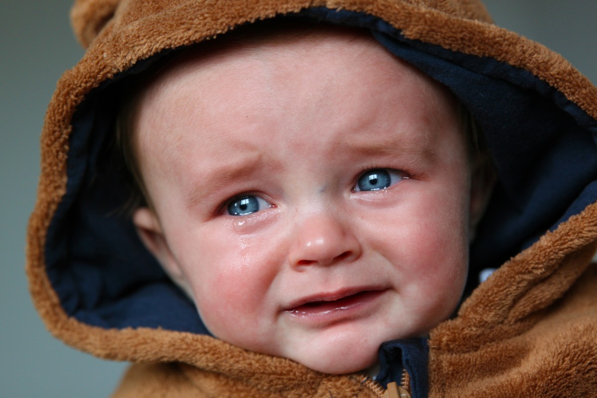 En la imagen puedes ver un bebé con un abrigo con gorrito marrón que está llorando