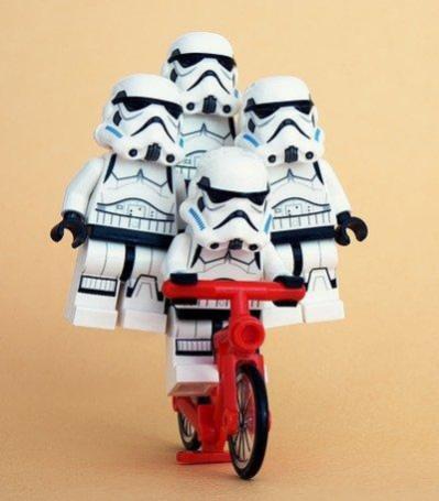 Cuatro muñecos de robots-soldado de "La guerra de las galaxias" se coordinan para montar una sola bicicleta entre todos.